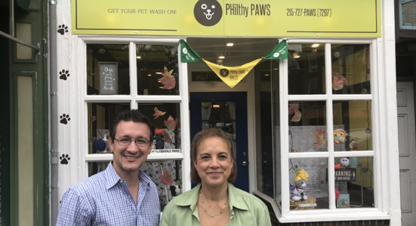 Philthy Paws owners pose outside of their storefront with the sign visible in the background.